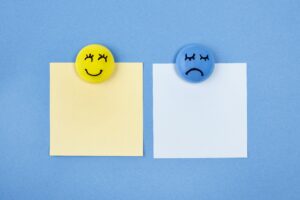 Karteczki przypięte do tablicy magnesami z uśmiechniętą i smutną miną. Ilustracja do artykułu odrzucanie pozytywów.