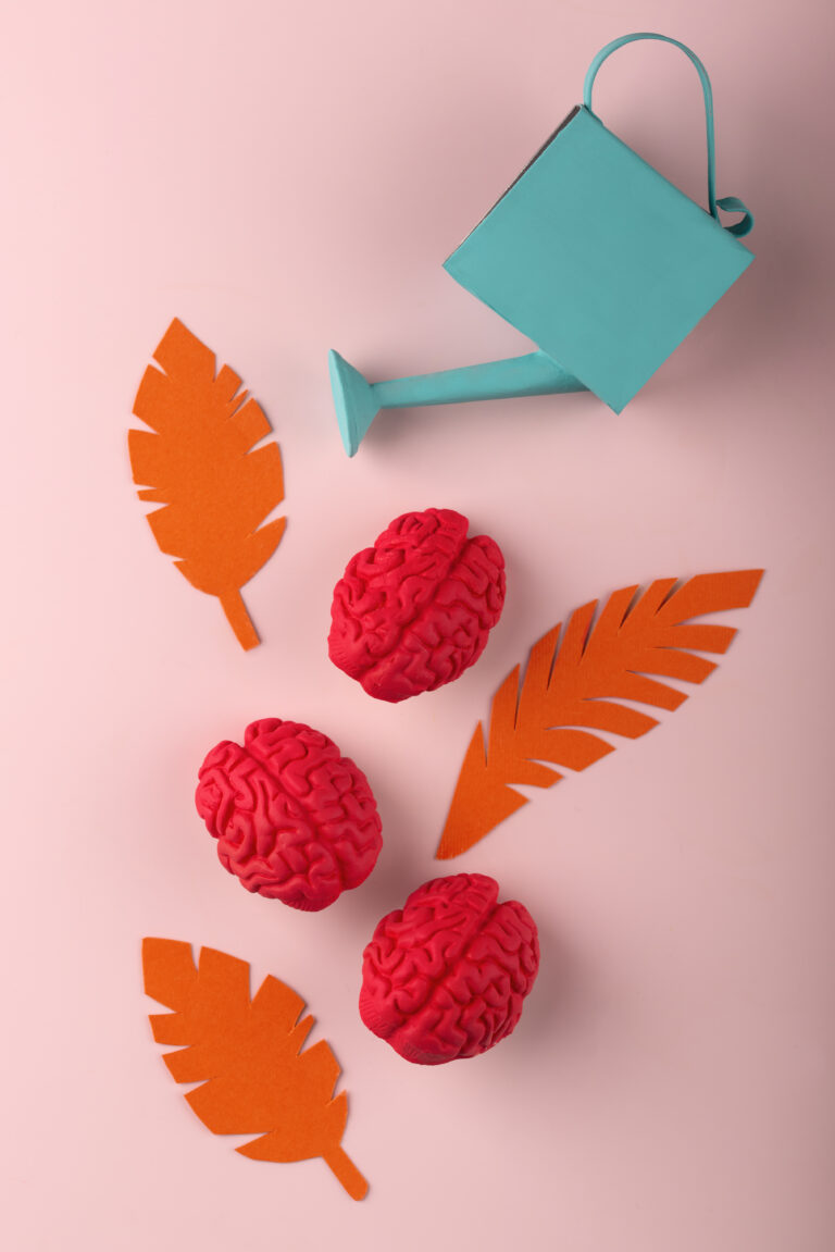 ADHD: październik miesiącem świadomości ADHD. Turkusowa konewka podlewa papierowe liście i pluszowe mózgi ułożone w kształt drzewa.