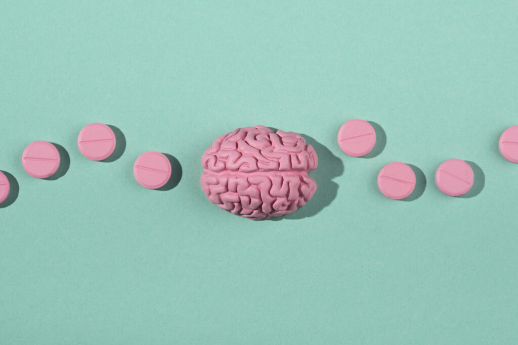 Atomoksetyna w leczeniu ADHD – grafika przedstawia różowy mózg i różowe tabletki na turkusowym tle.